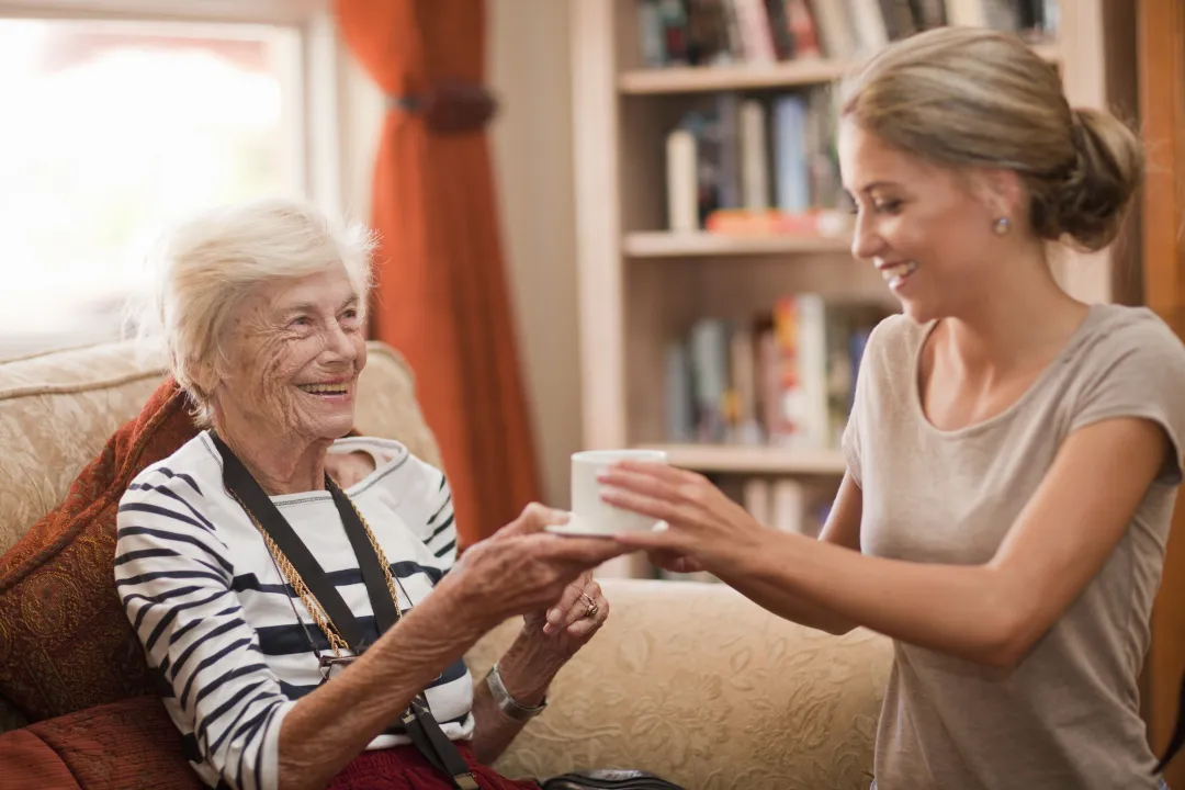 Carer serving tea to an elderly woman